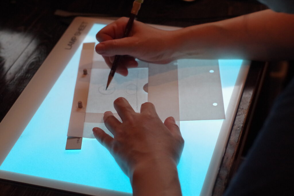 ライトボックスのうえにタップ(作画用紙を固定するためのアニメの道具)を置き、鉛筆で絵を描いている様子の写真