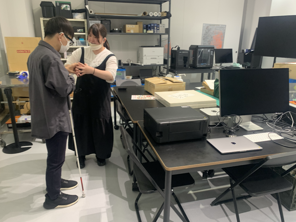 CCBT探検中の森さんの様子。場所はテックラボ。CCBTにあるデジタルファブリケーション機器など説明を、触手話でCCBTインターンの多田さんから伝えている。