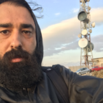 フード付きのジャケットを着た、厚いヒゲを持つ男性の写真。