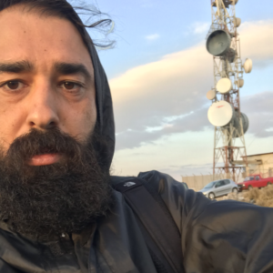 フード付きのジャケットを着た、厚いヒゲを持つ男性の写真。
