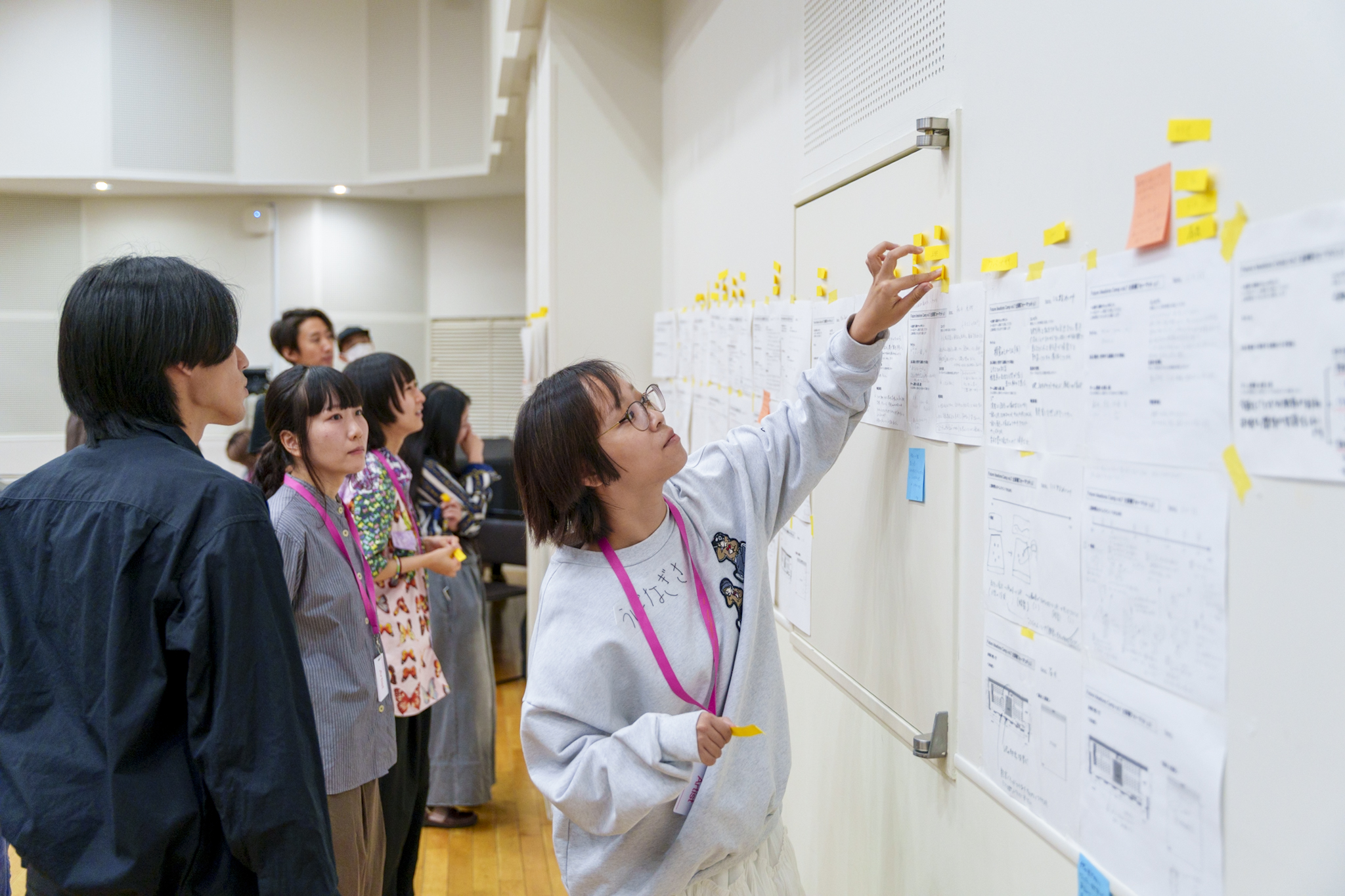 参加者が壁に貼られた企画書に付箋を貼りながら投票している様子の写真。